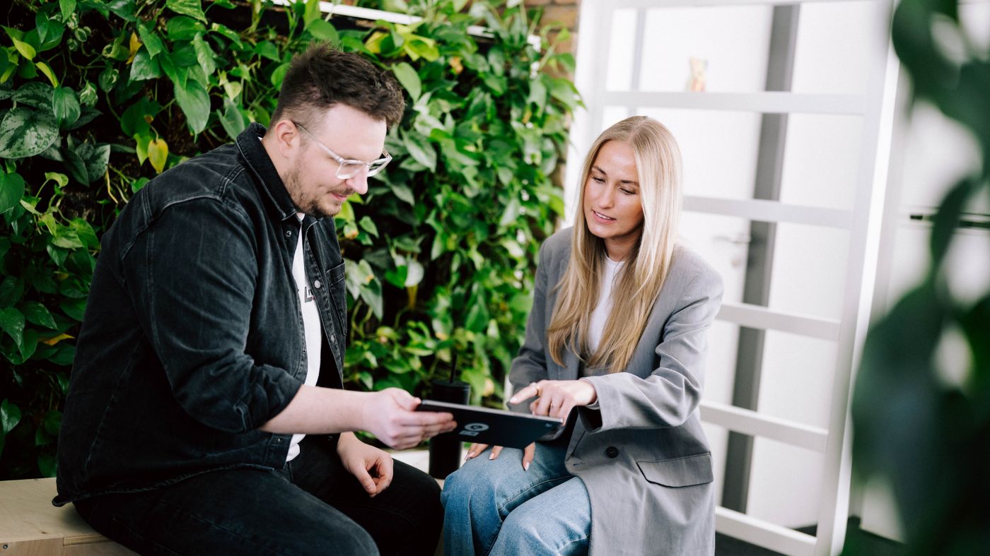 Digital Marketing Tipps Zwei Fachleute arbeiten an einem Tablet, umgeben von Grün in einem modernen Arbeitsraum