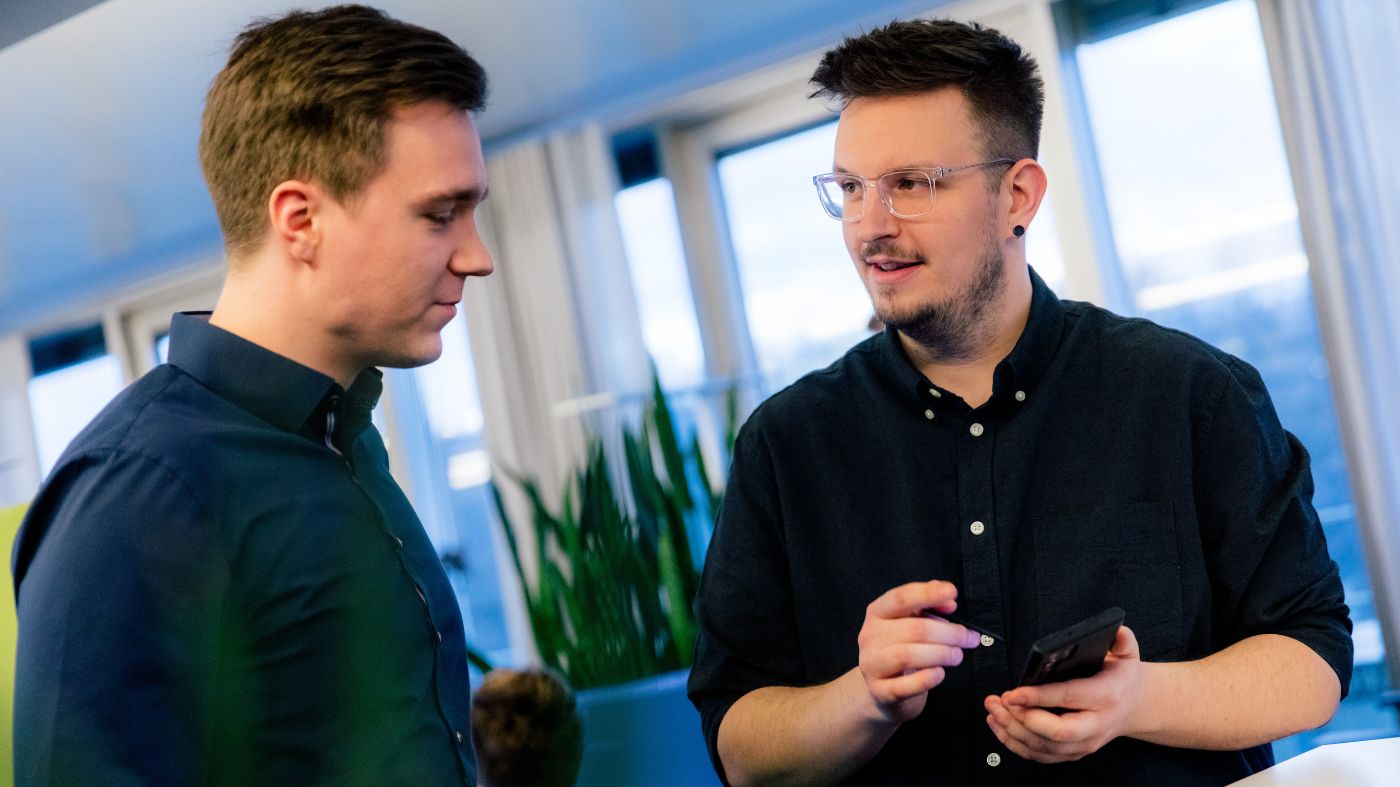 Instagram Stories Zwei Personen stehen in einem modernen Büro und unterhalten sich. Eine Person hält ein Smartphone in der Hand