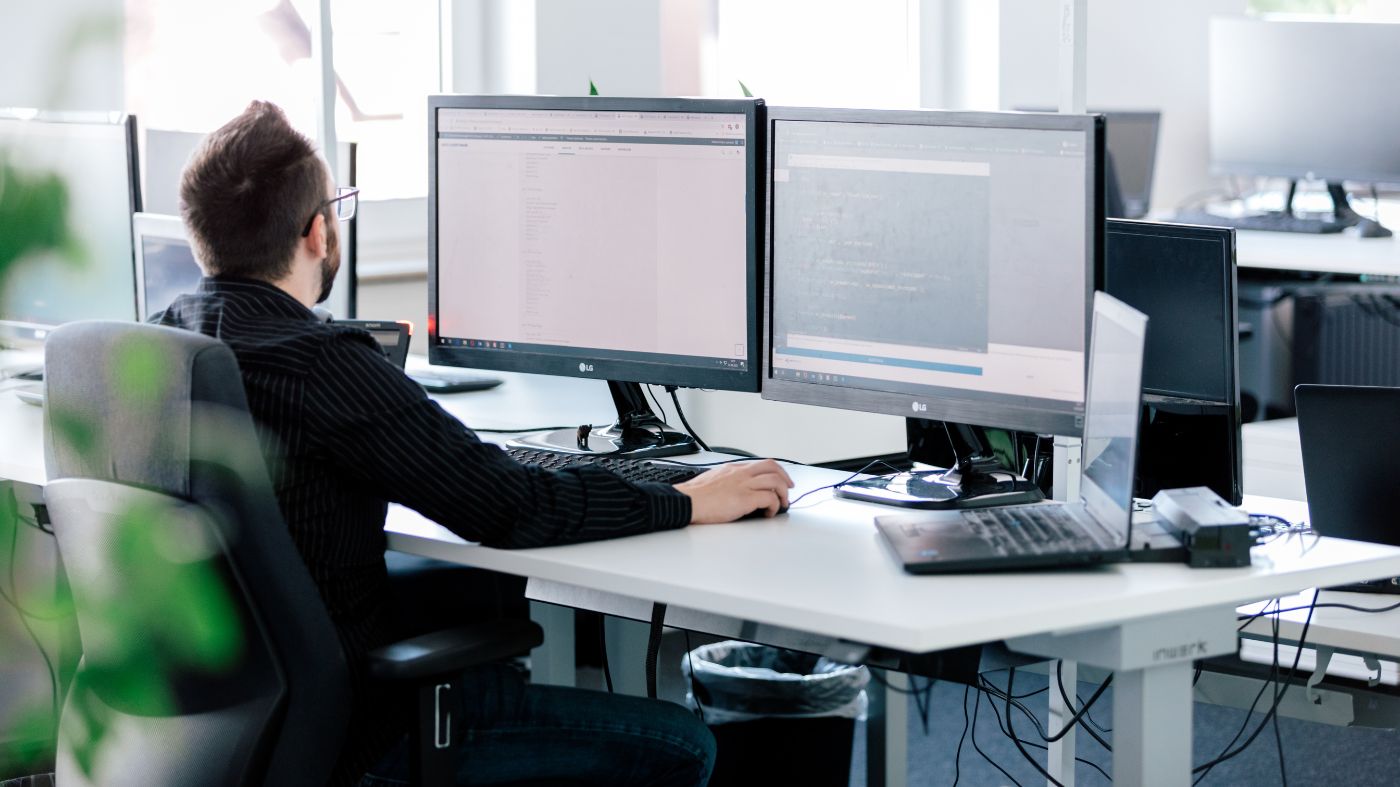 Beste Online Marketing Plugins für wordpress Ein Mann in einem Büro sitzt am Schreibtisch vor zwei Bildschirmen