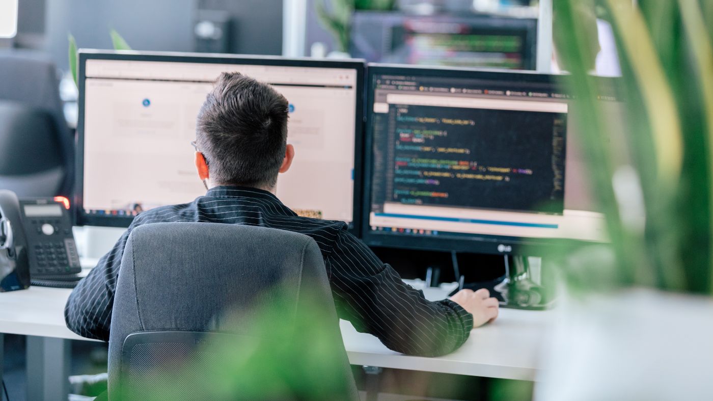 Seo Trends die Ihr Unternehmen beeinflussen Ein Mann sitzt am Schreibtisch vor zwei Monitoren. Er ist von hinten Fotografiert.