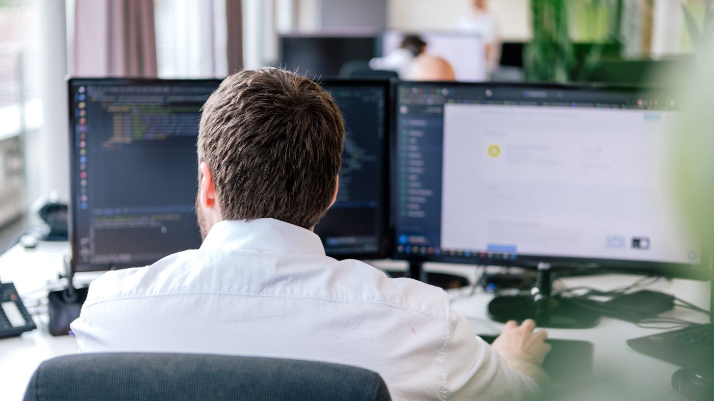Was Sie mit Ihrem Content tun sollten. Ein Mann sitzt am Schreibtisch vor zwei Monitoren. Er wird über die Schulter fotografiert